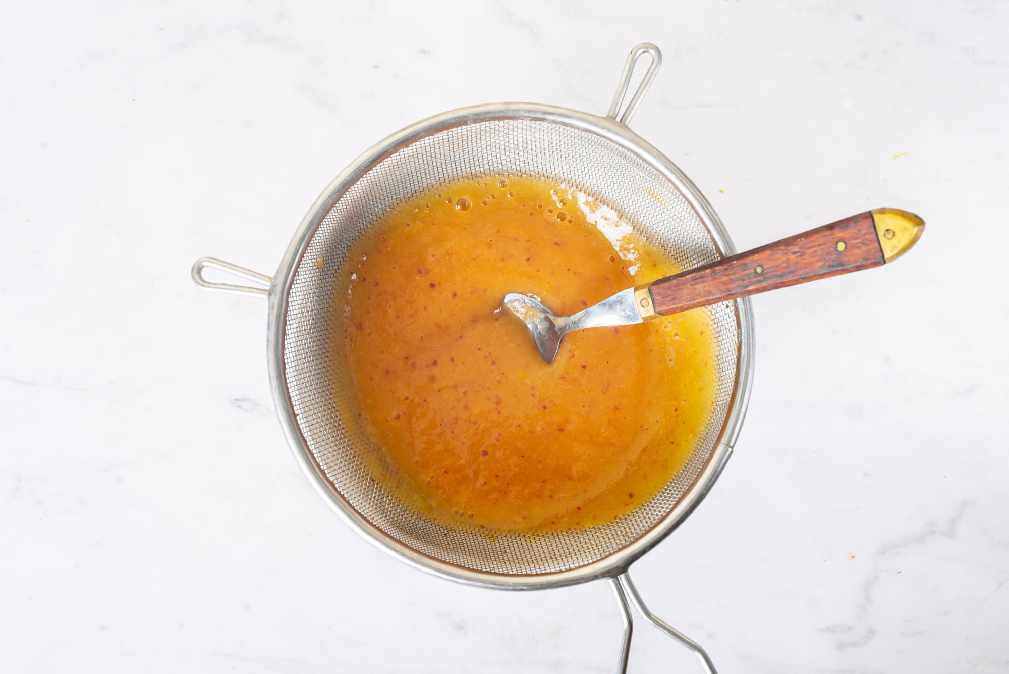 Peach puree in a strainer with a spoon.