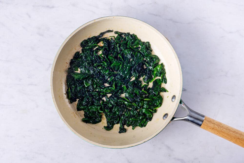 a skillet with sauteed spinach in it.