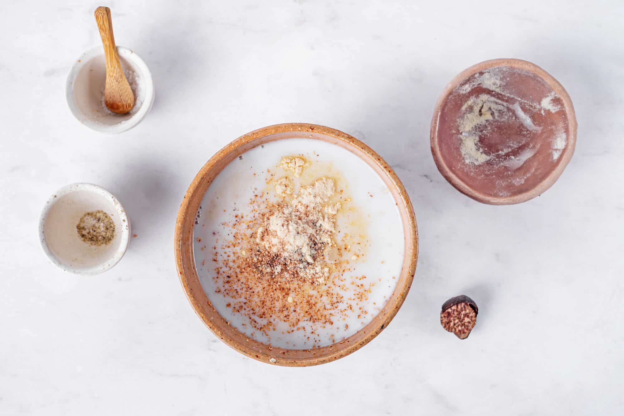 ingredients-for-scalloped-potatoes-in-bowls-mixed-into-center-bowl-heavy-cream-salt-pepper-garlic-powder-nutmeg-thyme