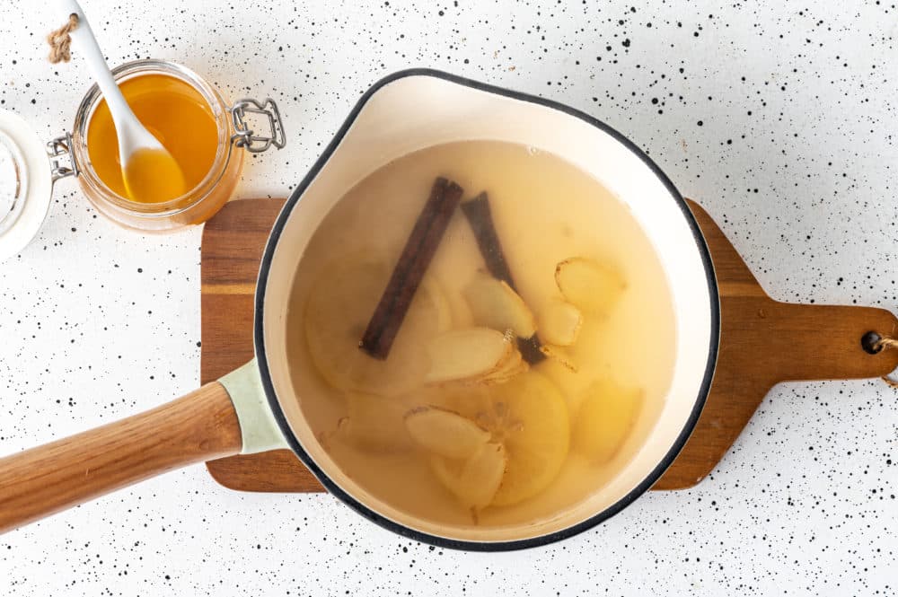 ginger tea in a pot on a wooden board with honey in a glass jar with a spoon on the side.