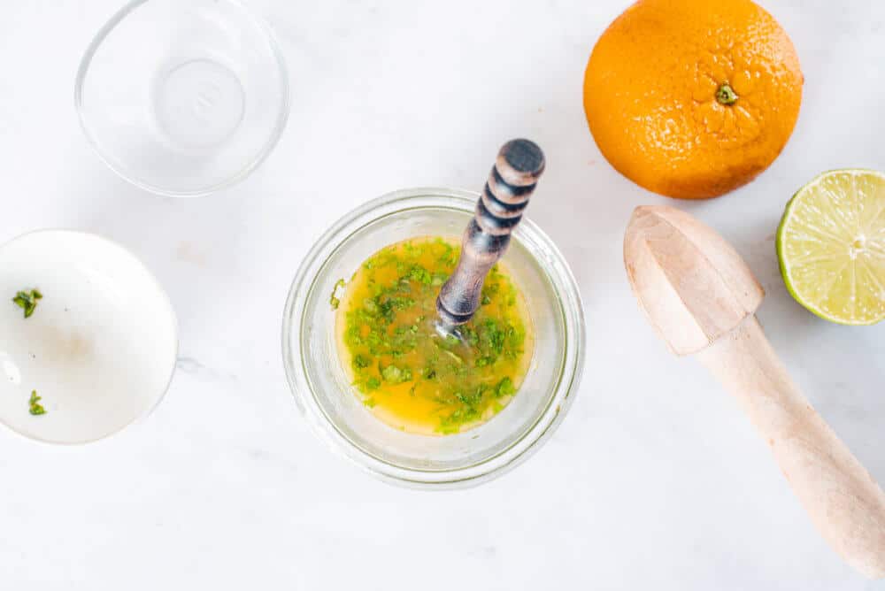 dressing in a glass bowl with a spoon with two empty bowls on the side and an orange.