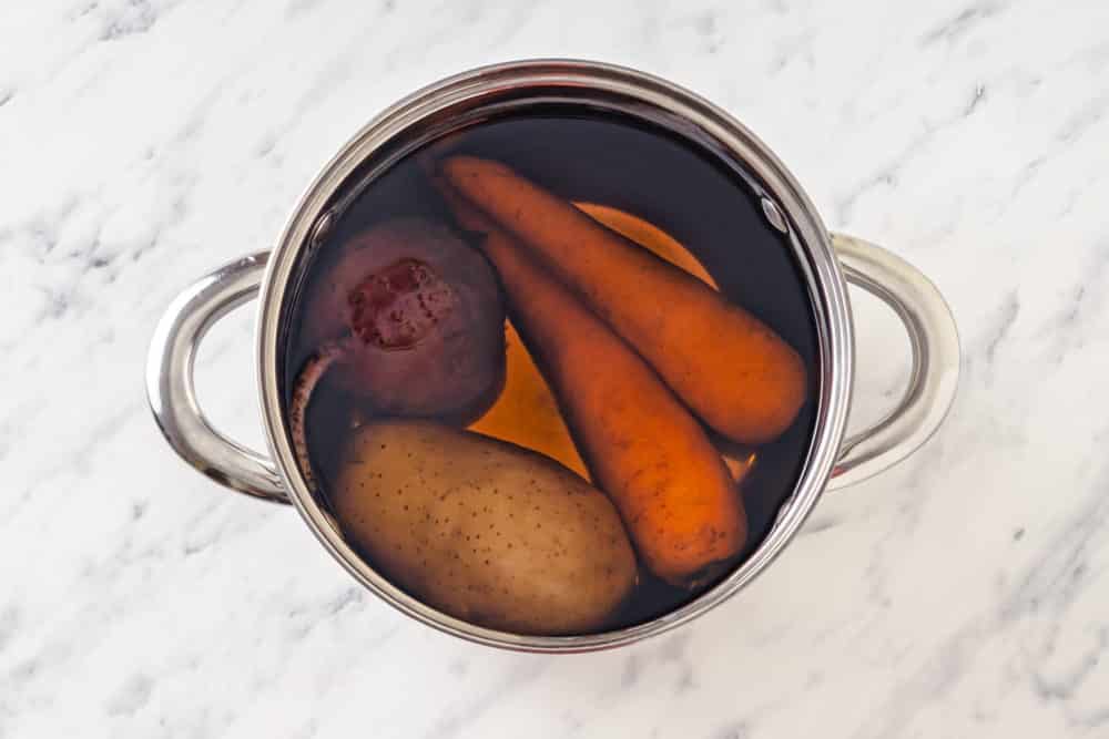 potato beet and carrots cooking in a silver pot filled with water.