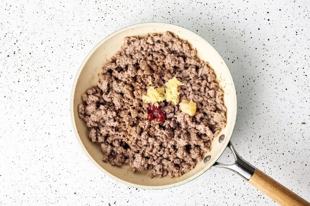 Ground turkey, garlic, ginger, and sriracha cooking in a skillet.