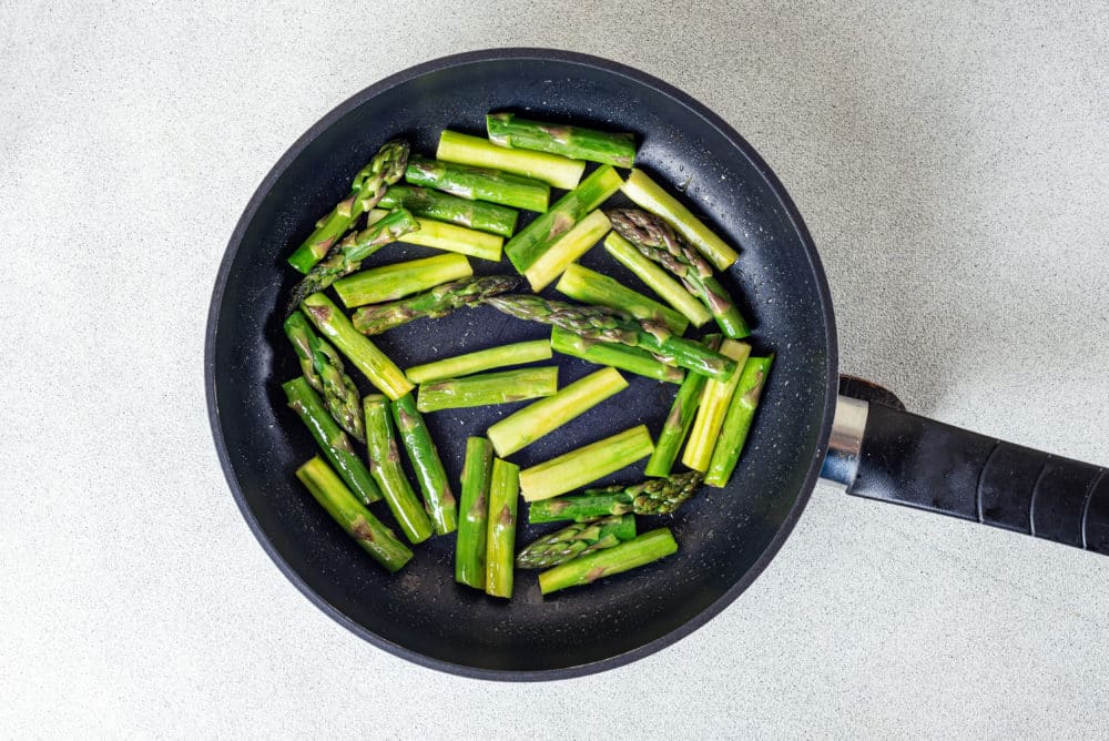 Chopped asparagus in a black skillet sauteing with olive oil.