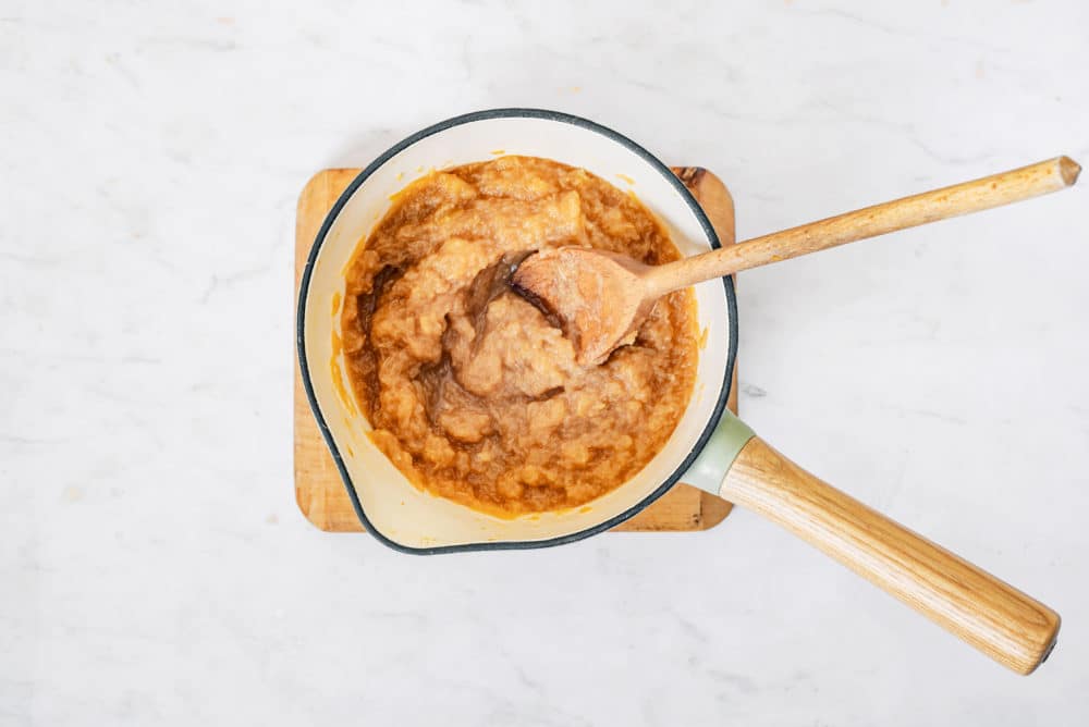 Stirring apple jam in a beige saucepan with a wooden spoon.