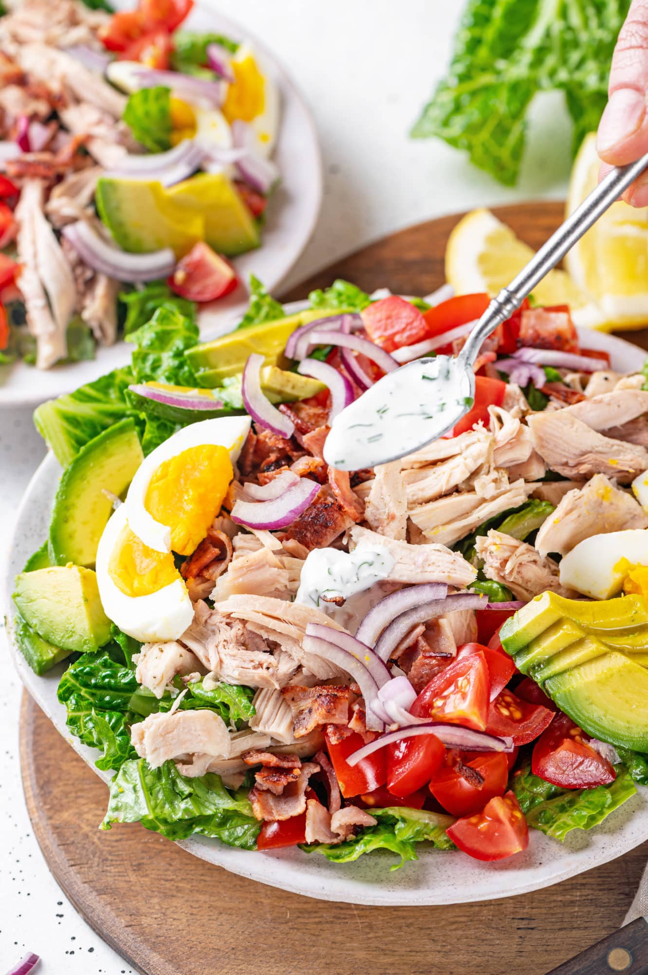 Chicken Cobb salad with ranch drizzling on top of the salad with a spoon.