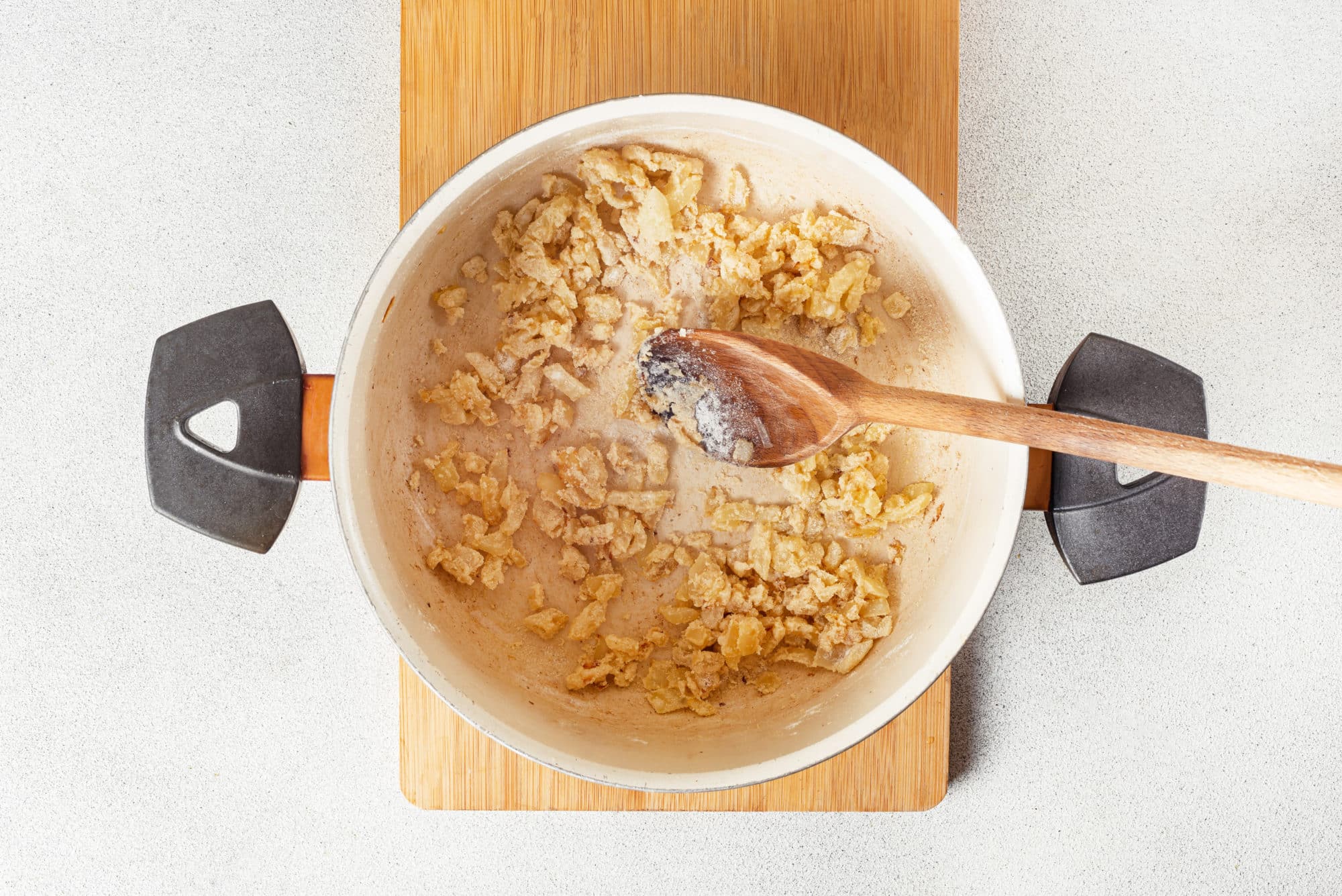 flour onion and garlic sauteing in a large soup pot with a wooden spoon.