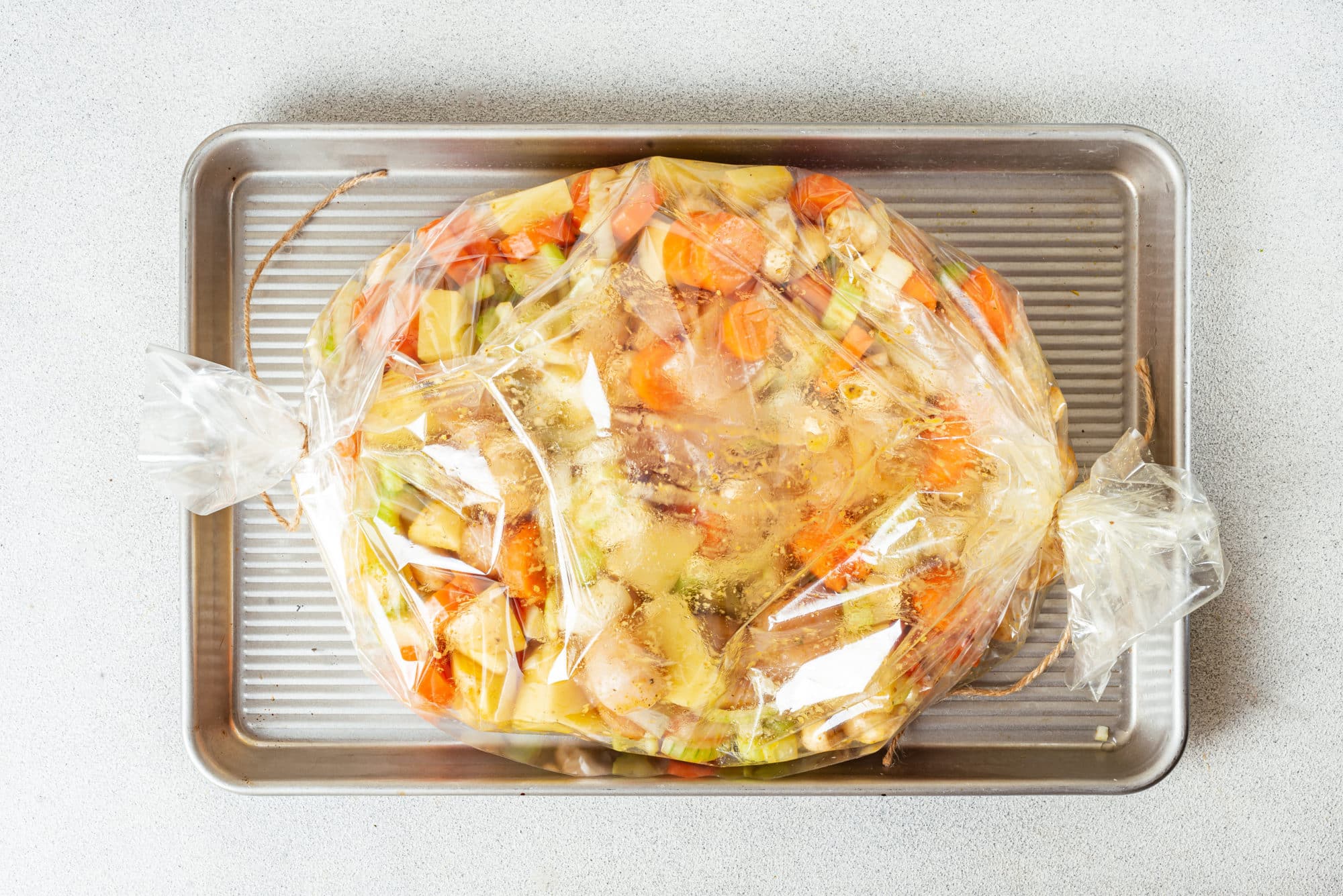 raw chicken and veggies in an oven bag on a baking sheet. 