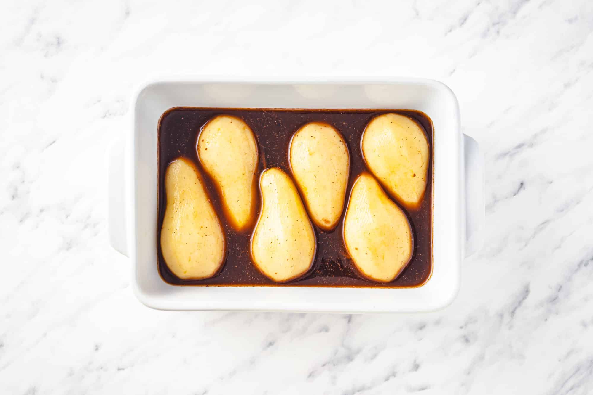 halved pears marinating in a honey spice mix in a baking tray.