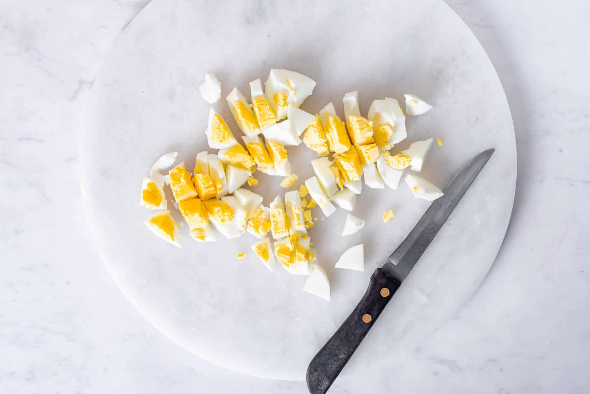 Chopped hard boiled eggs on a board with a knife.