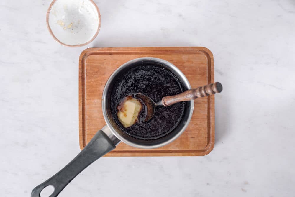 cooking caramel in a pot with a spoon on a wooden board with an empty butter bowl on the side.