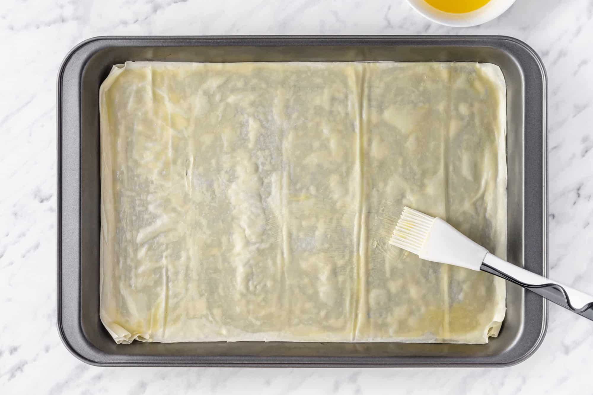 phyllo dough in a baking tray brushed with butter with a brush on the side.