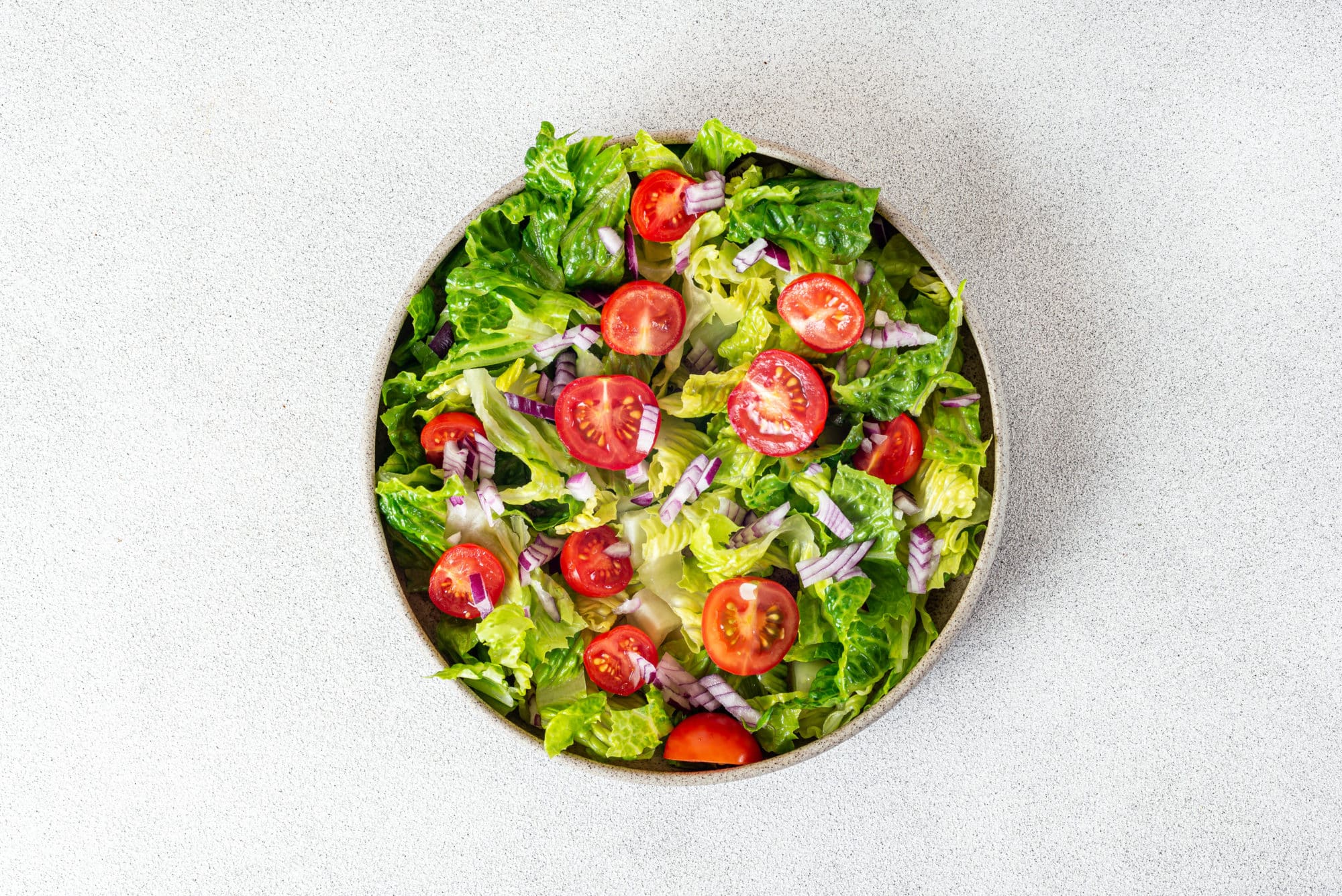 lettuce tomatoes and red onion in a grey bowl.