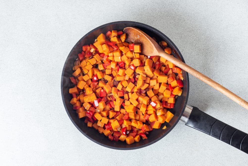 A black skillet with a wooden spoon red pepper and sweet potatoes.