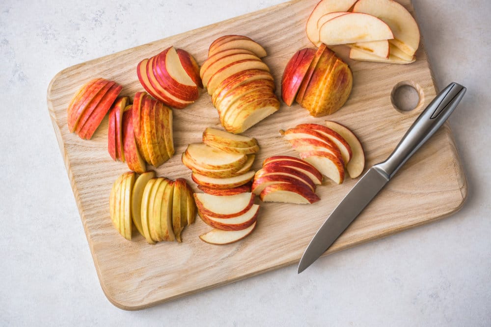 a wooden board with a knife and sliced apple slices on it.