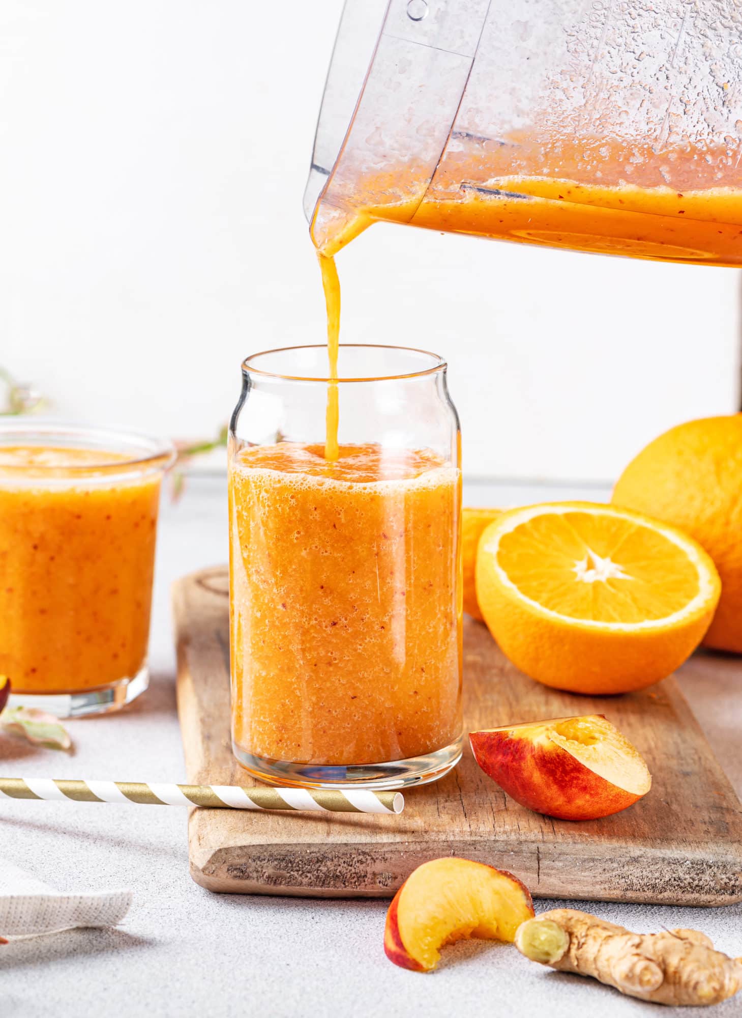 a smoothie being poured into a glass from a blender on a wooden board with orange halves.