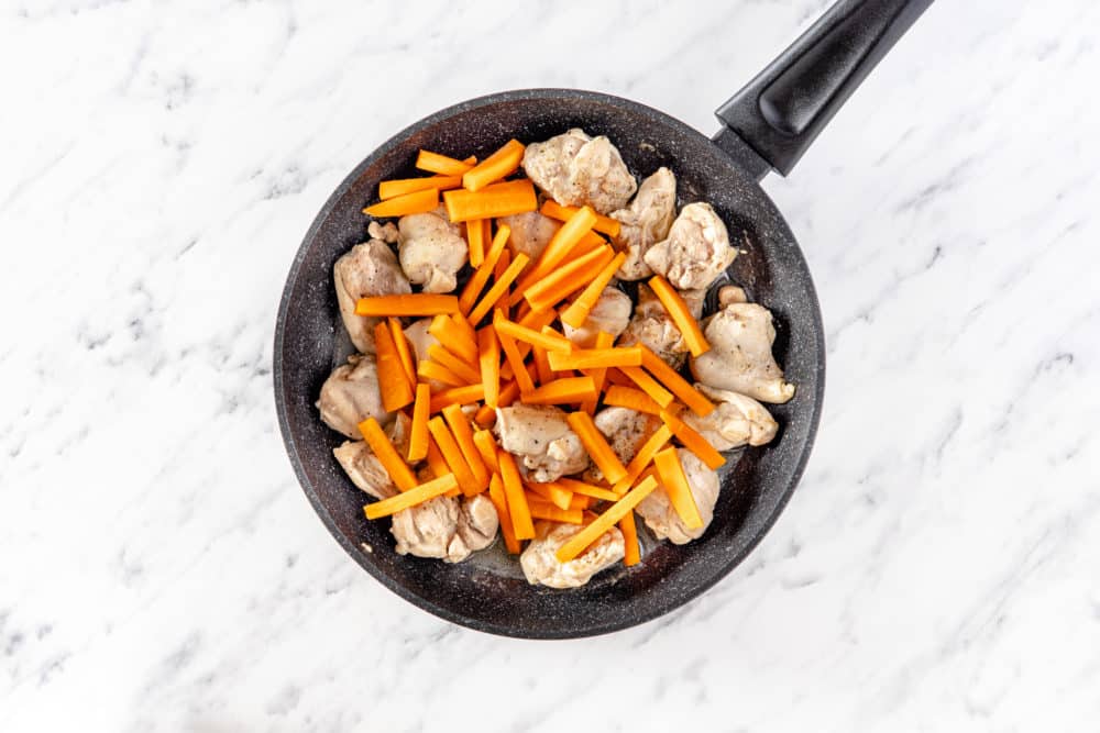 a black pan with chicken and chopped carrots.