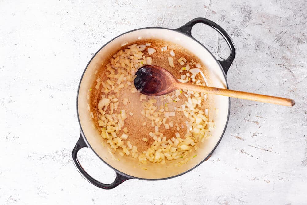 Onions sauteing in a soup pot with a wooden spoon.