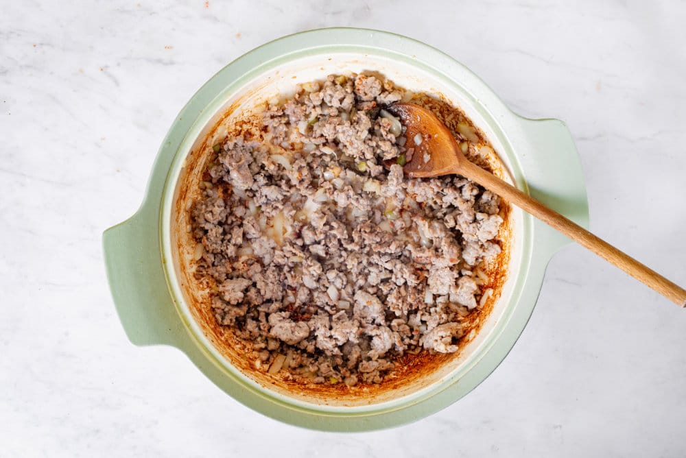 Sausage sauteing in a green soup pot with a wooden spoon.