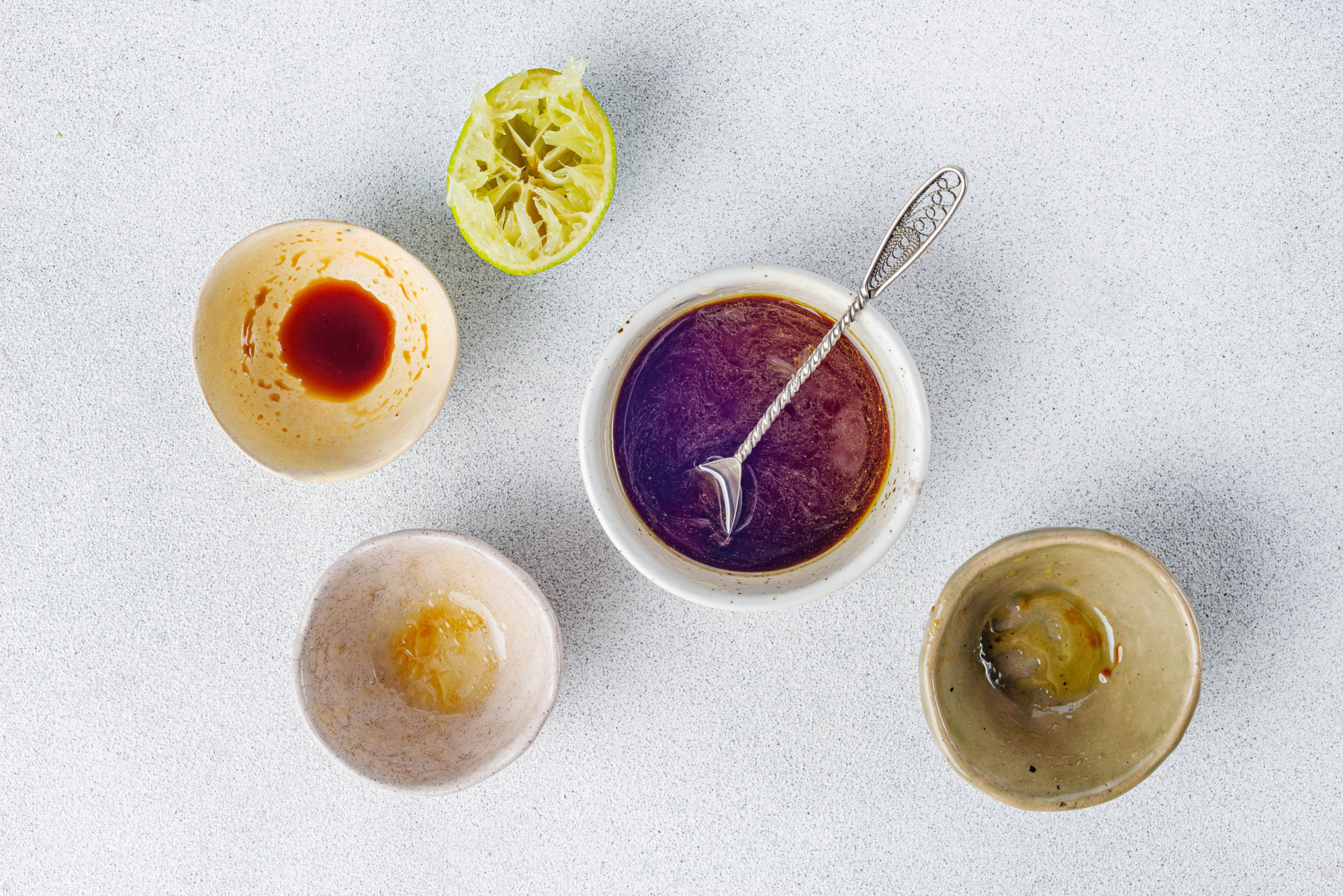 Sesame dressing ingredients in bowls with dressing in the center bowl mixed with a spoon.