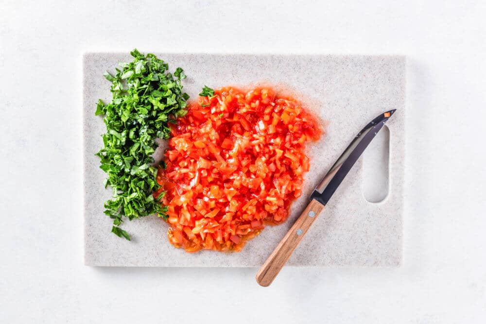 Chopped tomatoes and parsley on a cutting board with a knife.