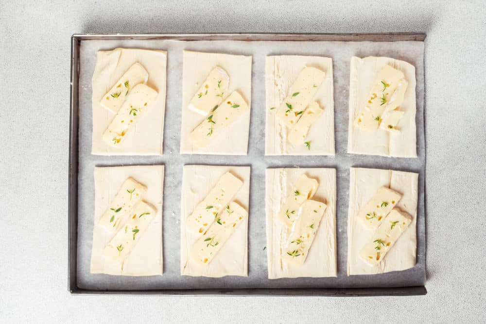 a baking tray with puff pastry sheets and slices of brie on the sheets.