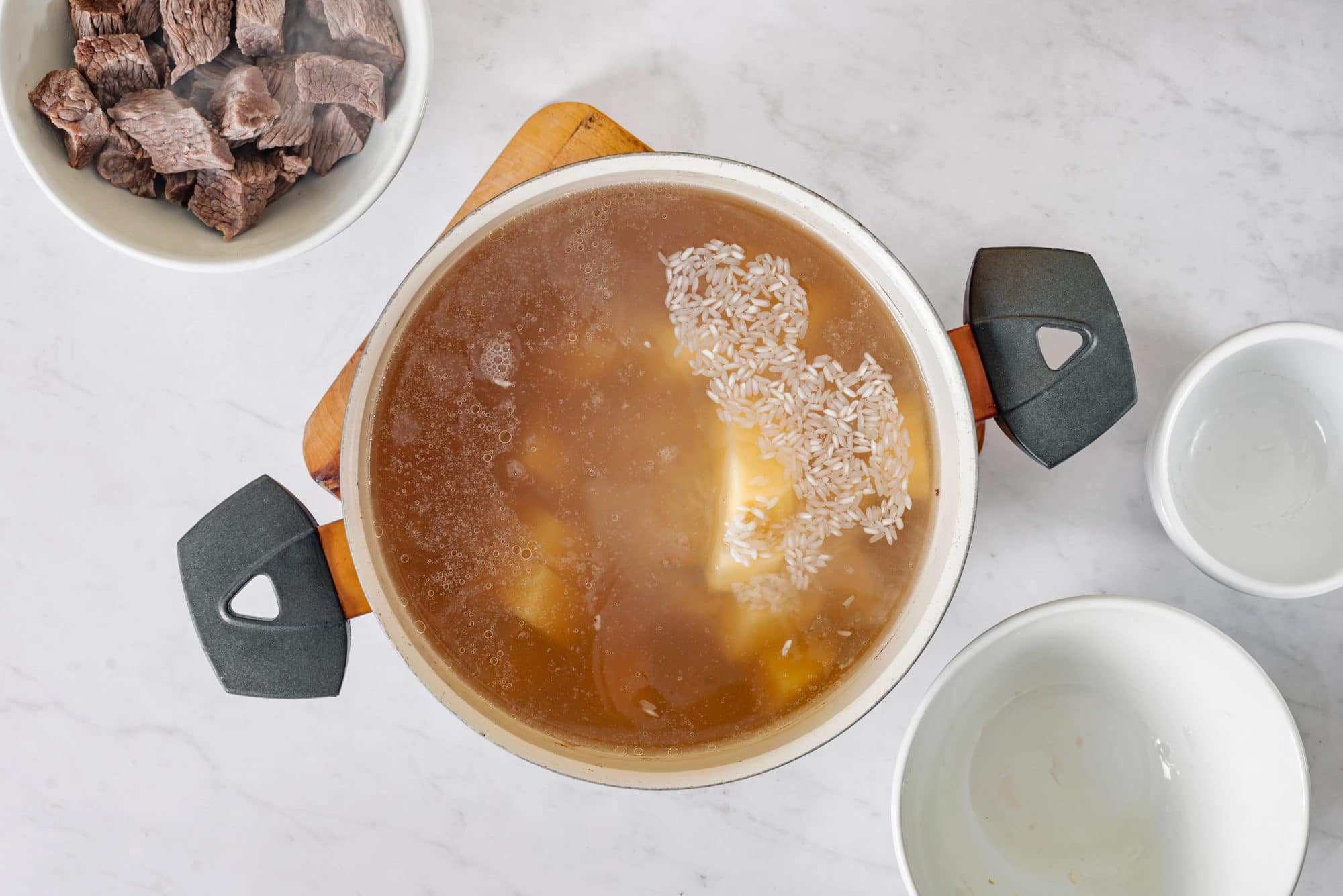 beef-soup-cooking-in-a-soup-pot-on-a-wooden-board-with-bowls-and-beef-on-the-side