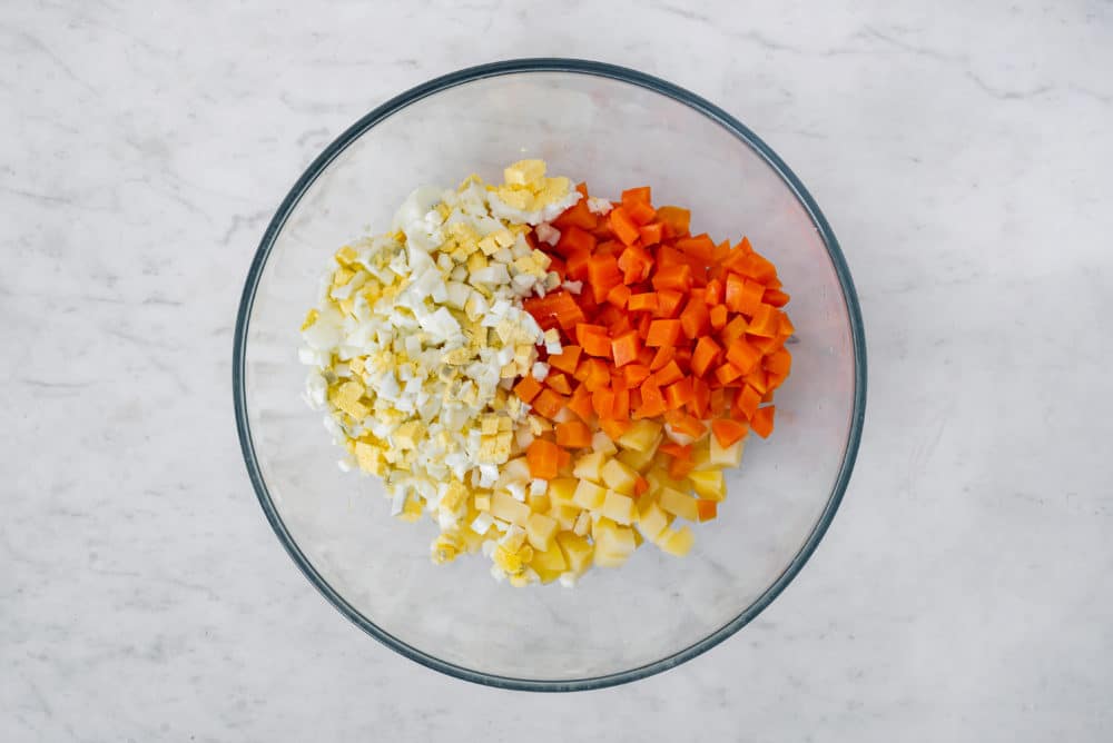 Chopped olivier salad ingredients in a glass bowl.