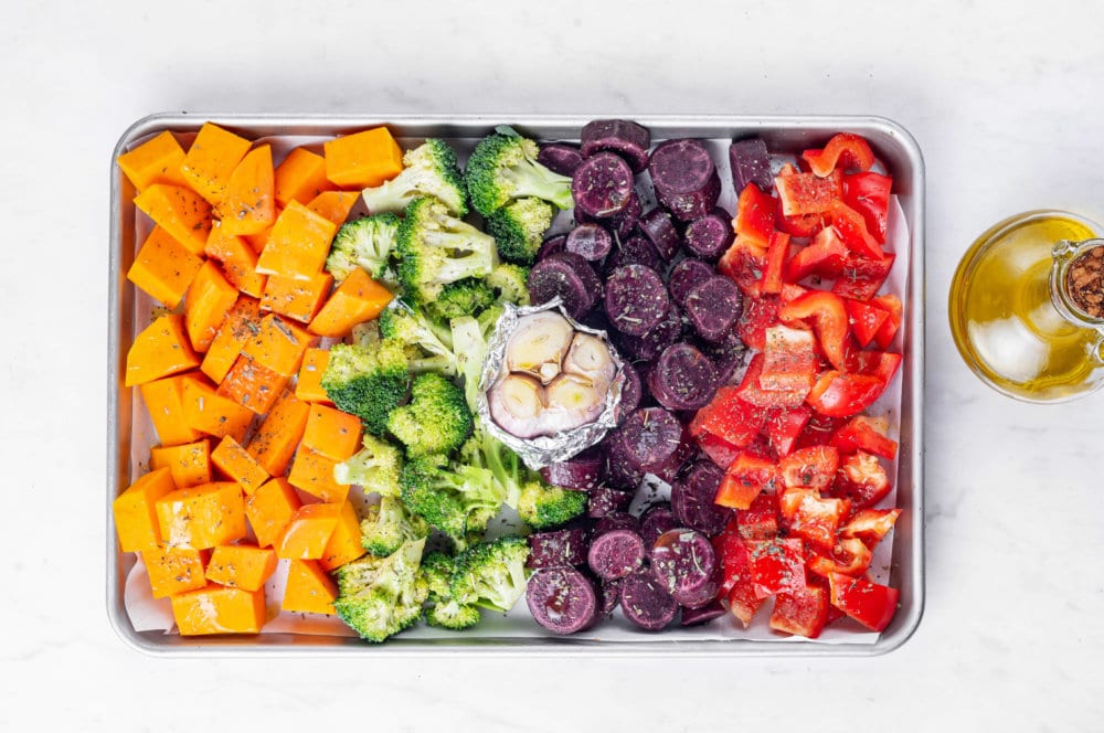 roasted veggies on a baking tray with roasted garlic wrapped in foil in the center.