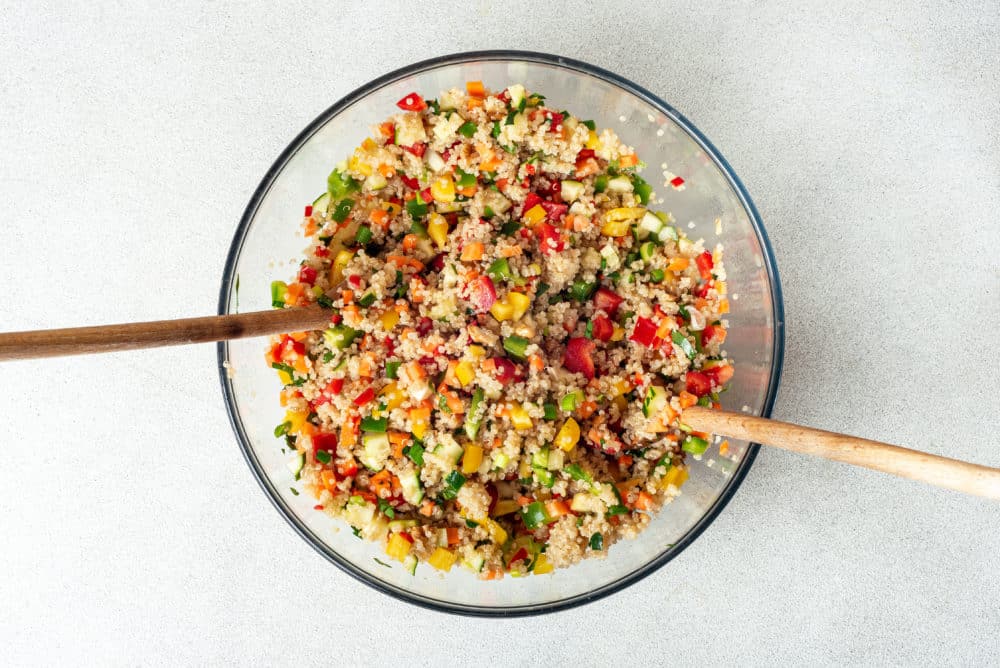 fresh salad ingredients prepared and mixed in a glass bowl with two wooden spoons.