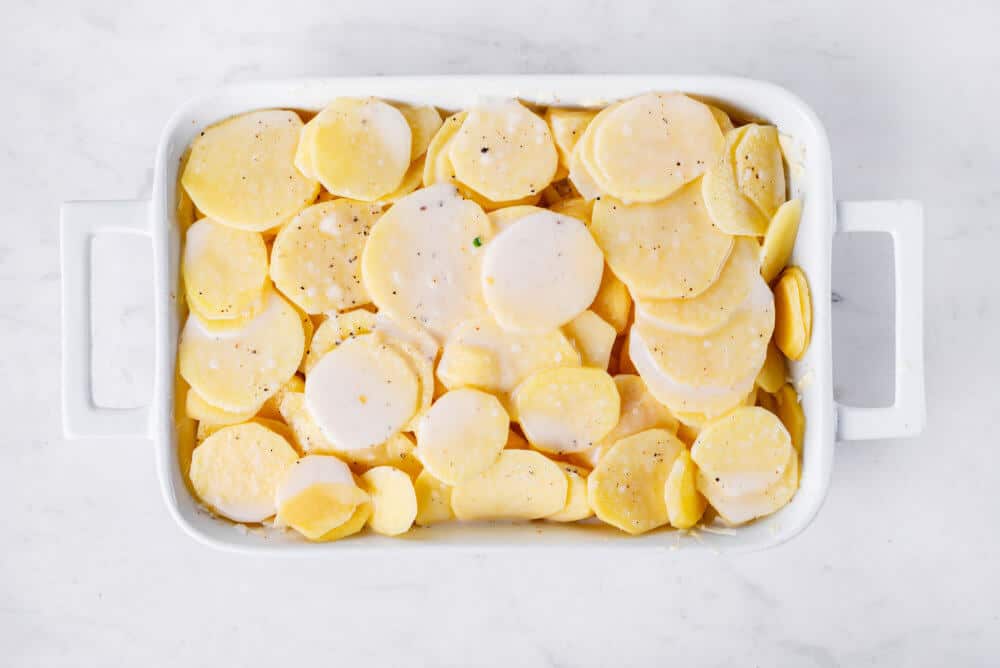 scalloped potatoes ready to bake in a white baking dish.