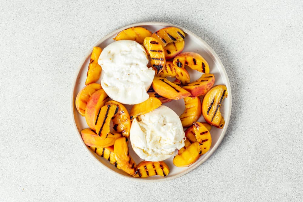 burrata cheese balls on a white plate with grilled peach slices.