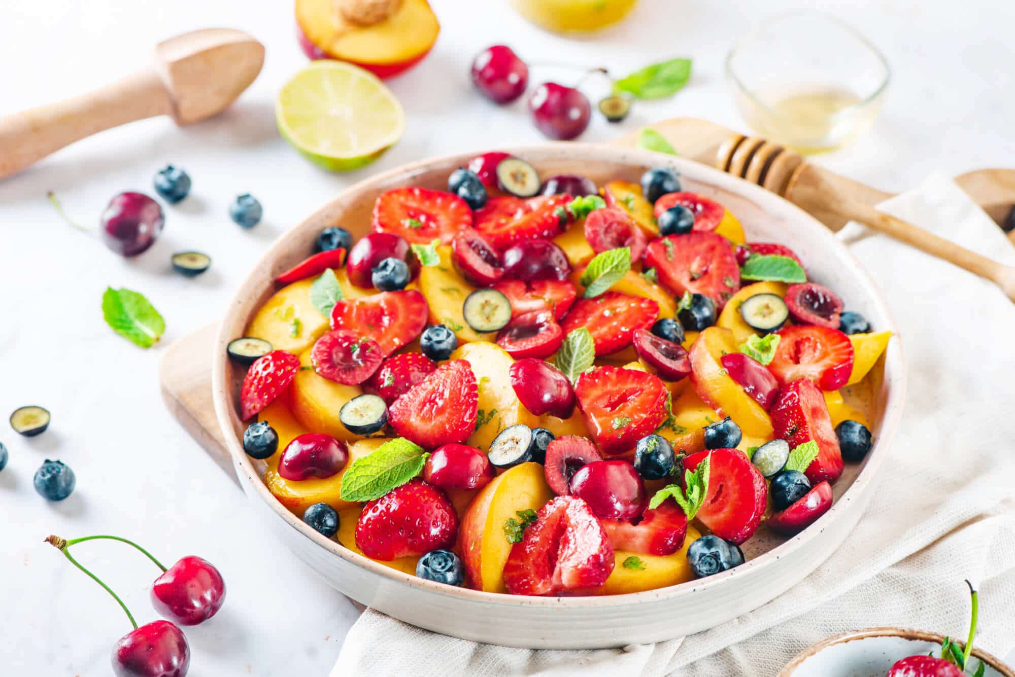 Summer fruit salad in a bowl with ingredients for the salad around.