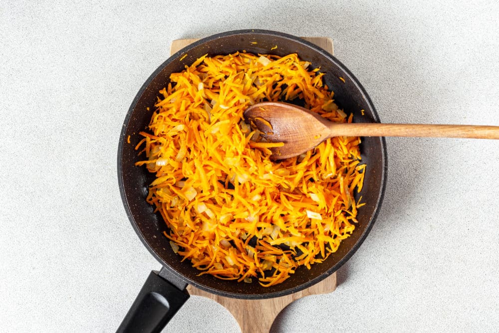 grated-carrots-in-a-skillet-on-a-wooden-board-with-a-wooden-spoon