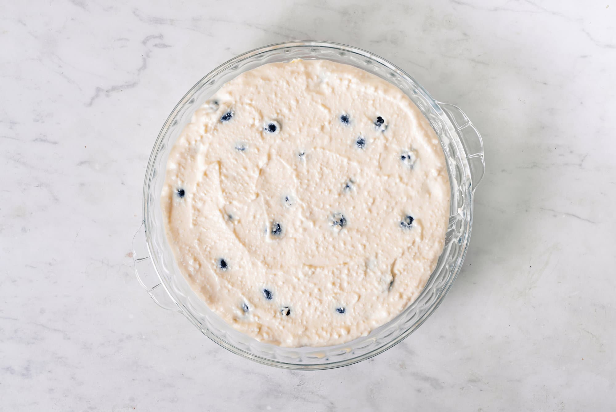 Raw blueberry cheese cake batter in a glass tray.