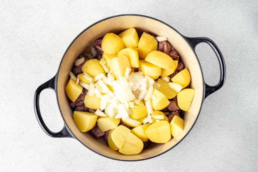 chopped potatoes onions and meat in a large black soup pot.