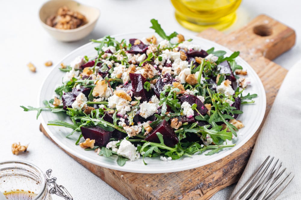 beet salad on a white plate on a wooden board with a fork on the side and olive oil in the background.