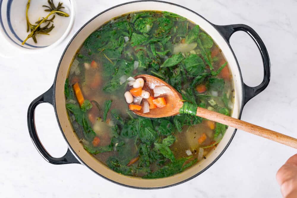 ingredients in a soup pot with greens on top.