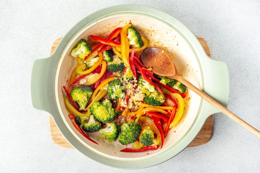 a pot filled with vegetables sauteing with a wooden spoon inside too.