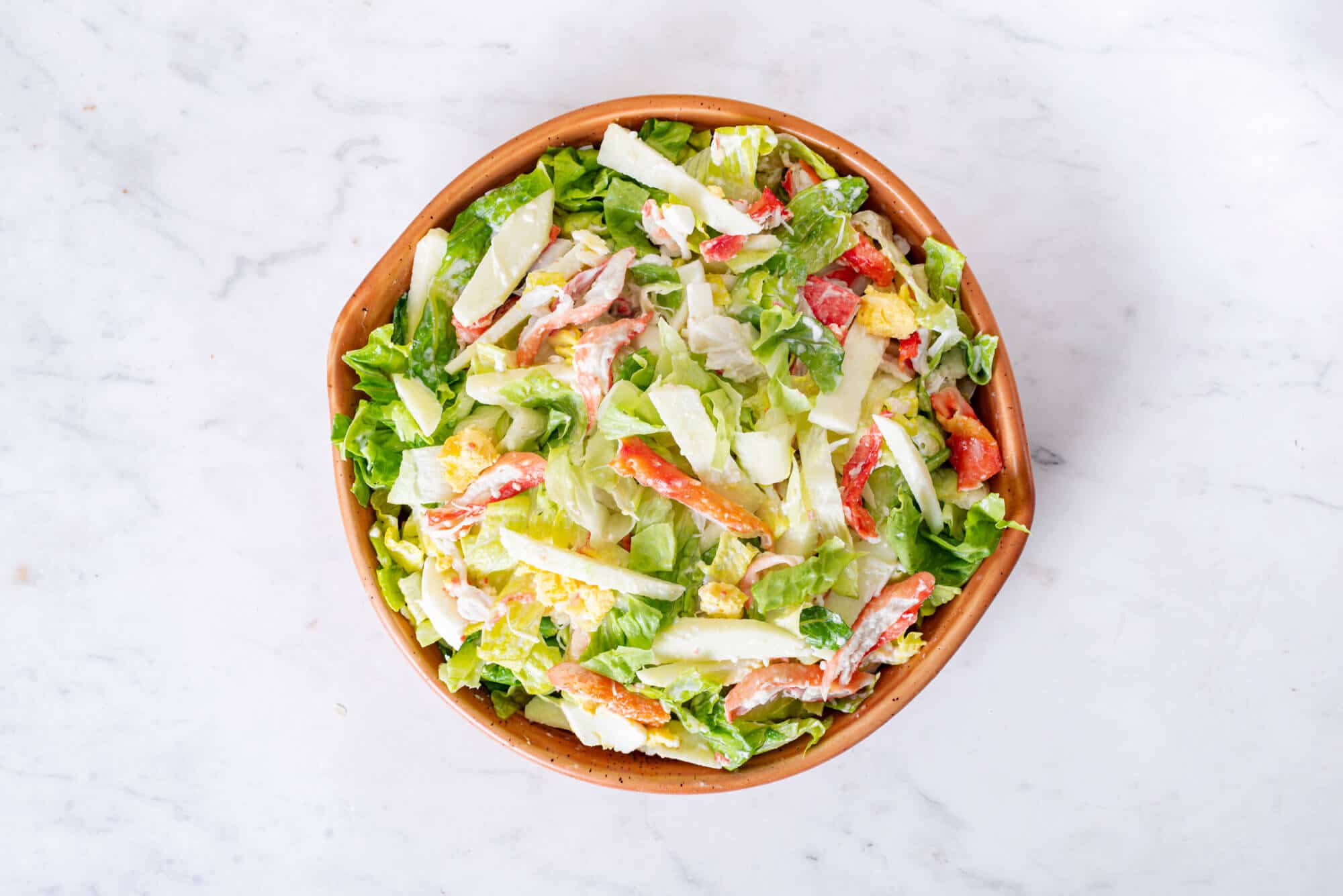 Crab apple salad ingredients combined in a brown bowl.