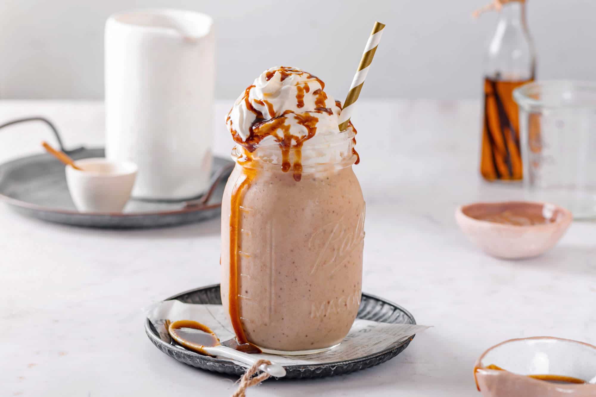 caramel-smoothie-in-a-mason-jar-with-a-striped-straw-on-a-black-plate-with-a-spoon