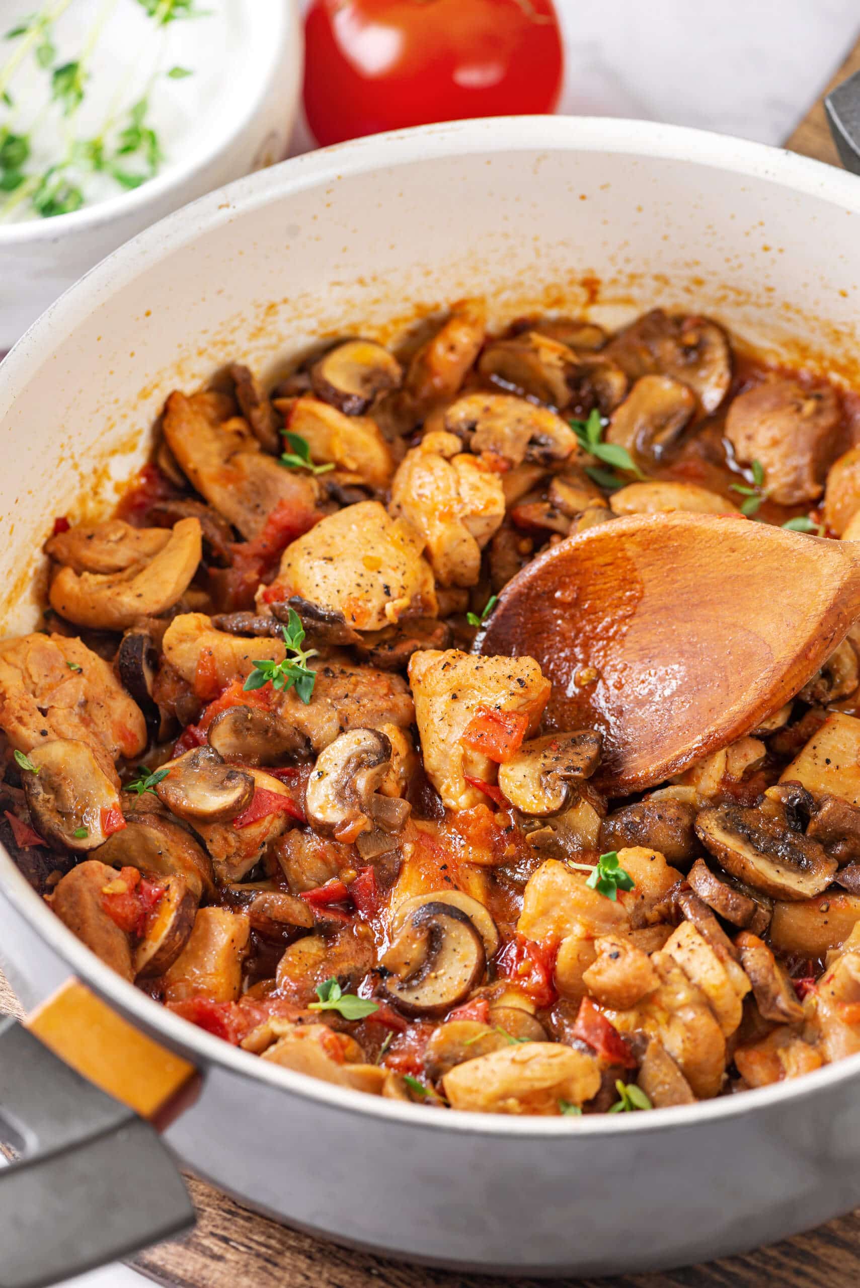 Chicken with mushrooms in tomato sauce in a pan with a wooden spoon.