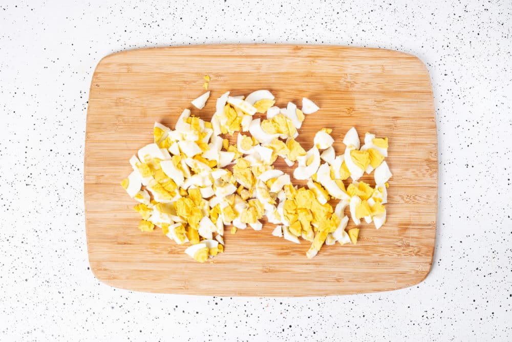 Chopped hard boiled egg on a wooden cutting board.