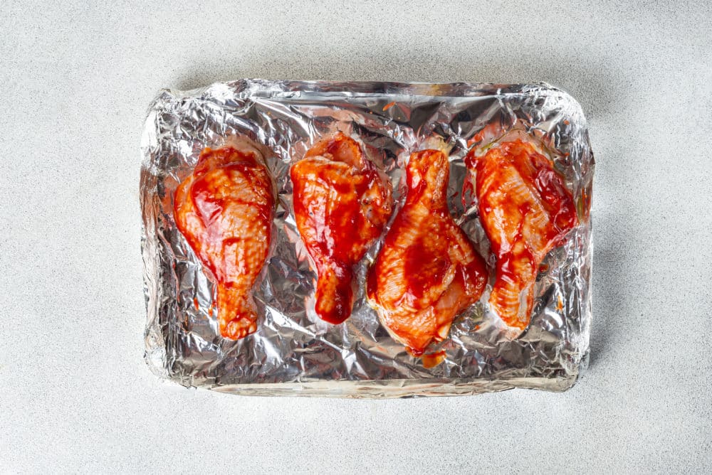 Chicken drumsticks on foil brushed with BBQ sauce.