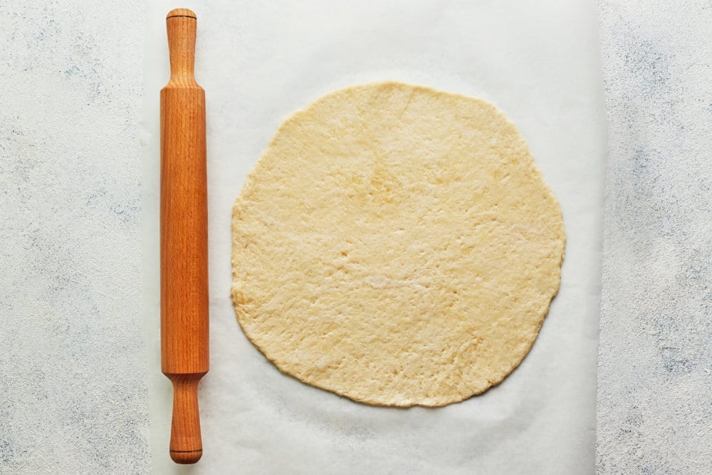 raw dough round with a rolling pin.