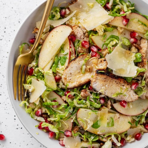 brussels sprouts salad put together with apples and pomegranate in a white bowl.