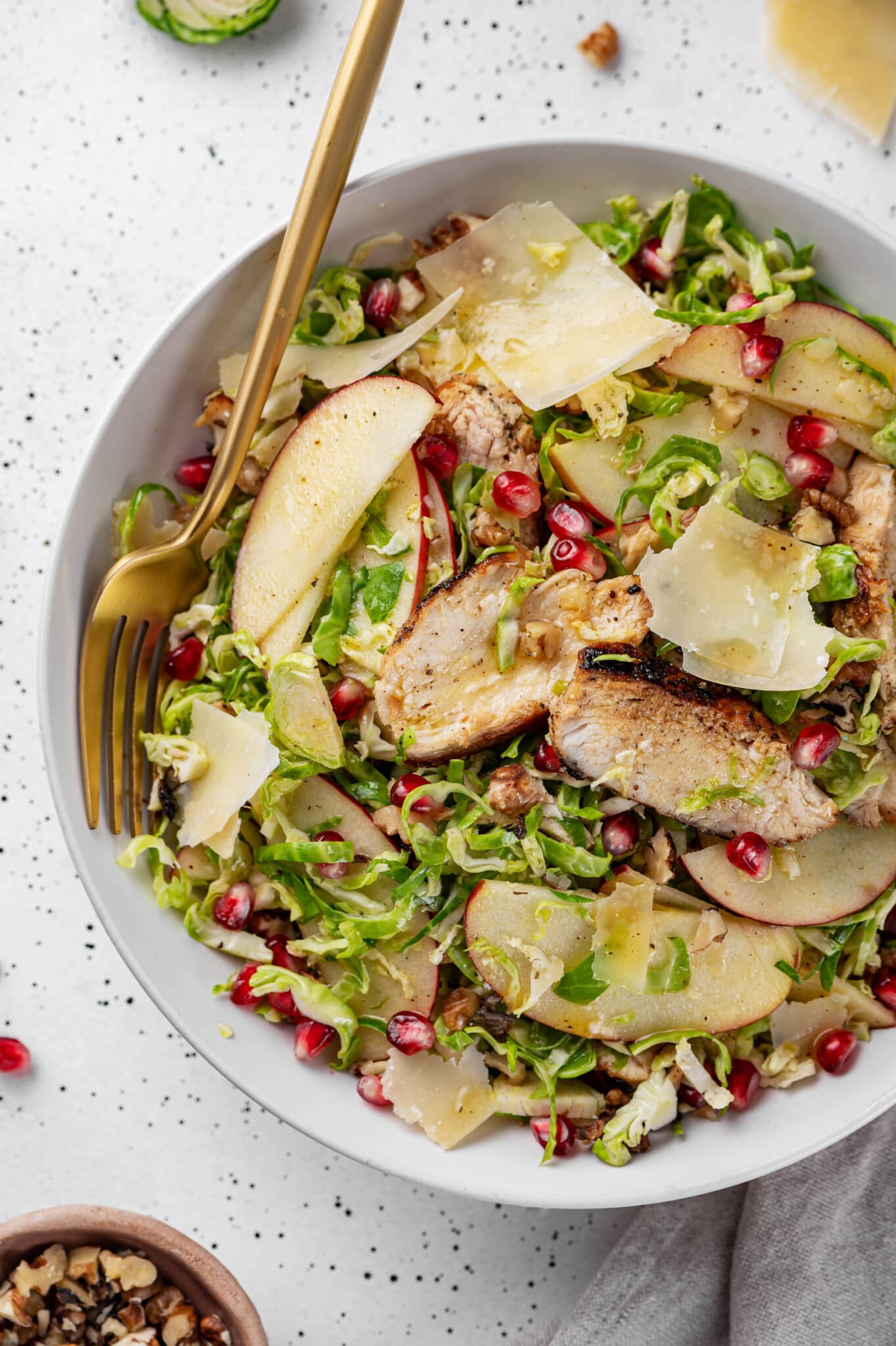 brussels sprouts salad put together with apples and pomegranate in a white bowl.