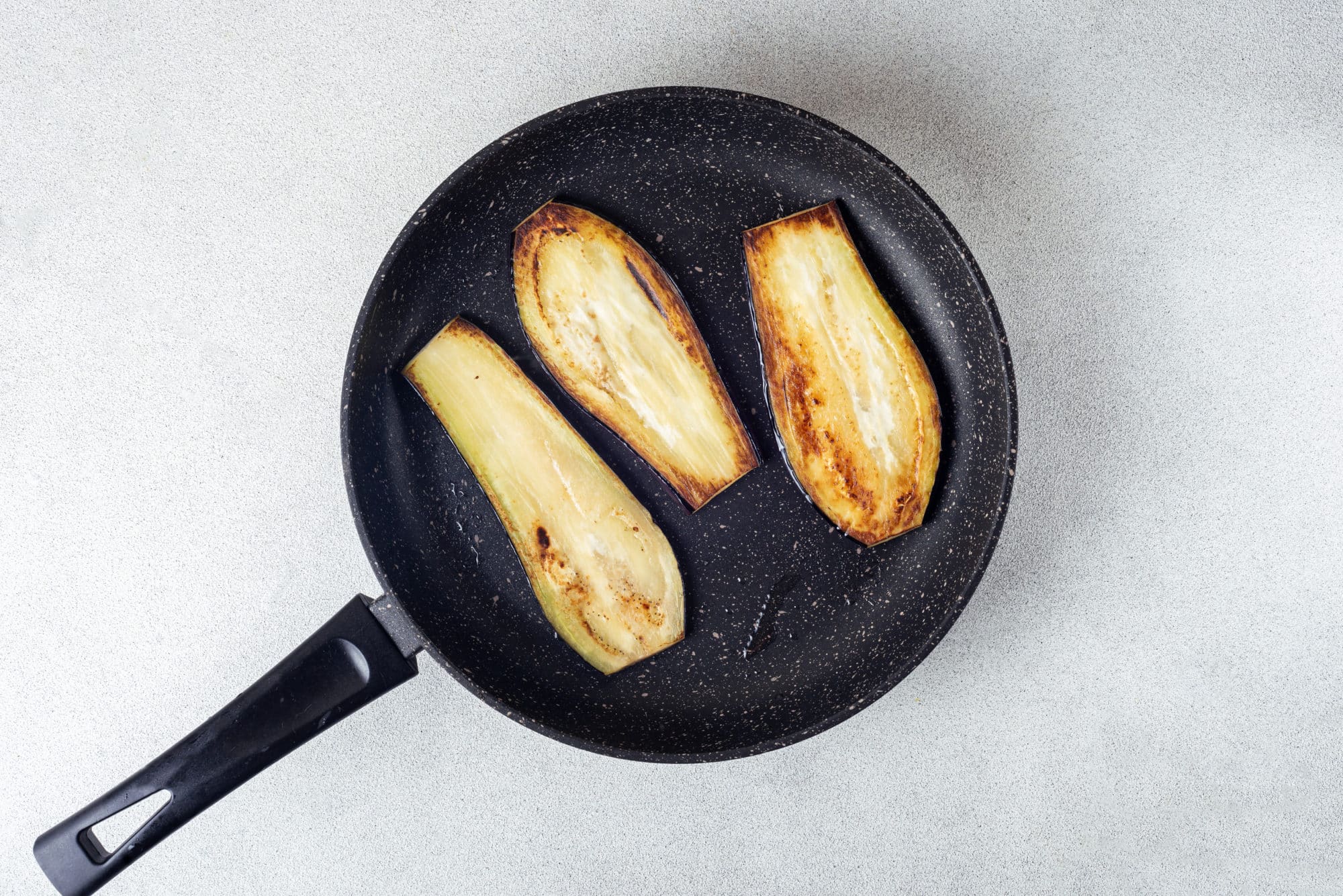 eggplant slices sauteing in a black skillet.