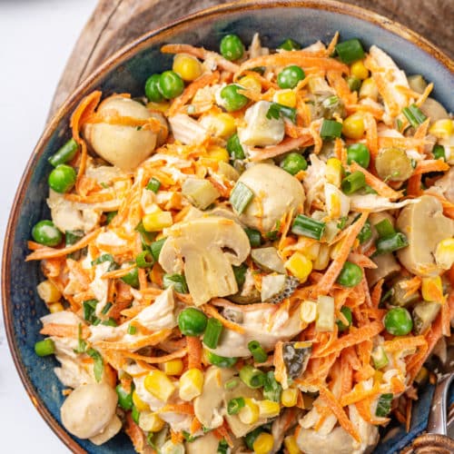 a blue bowl with a brown rim resting on a wooden board the bowl is filled with chicken mushroom veggie salad.