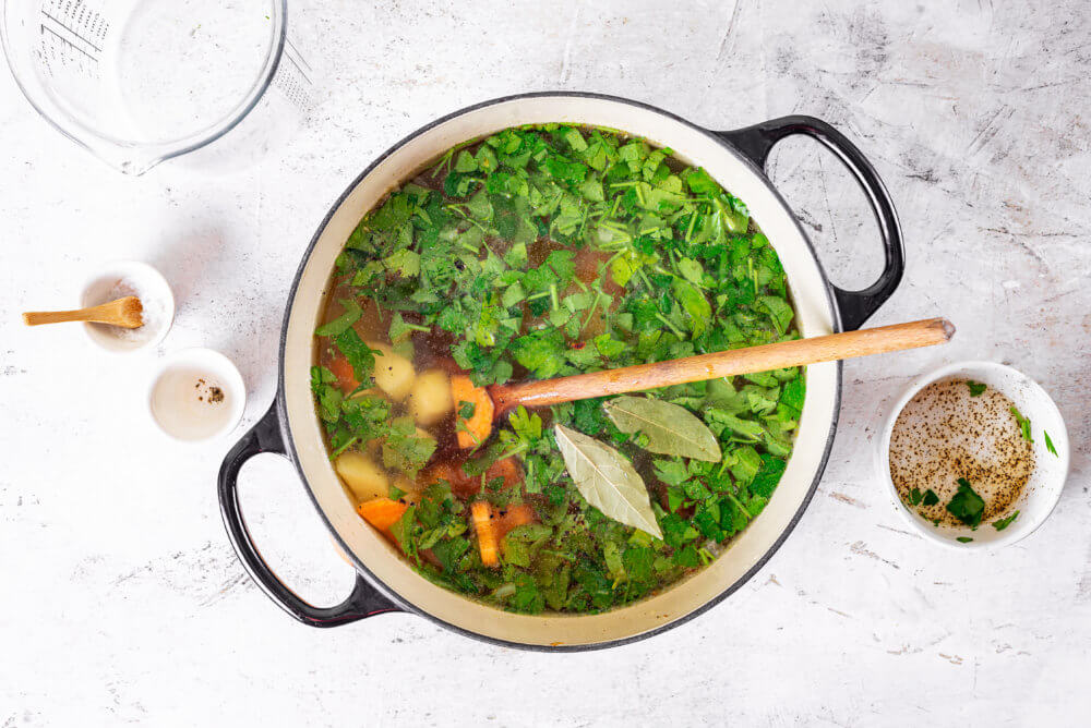 Sorrel soup in a large soup pot with a wooden spoon mixing the ingredients.